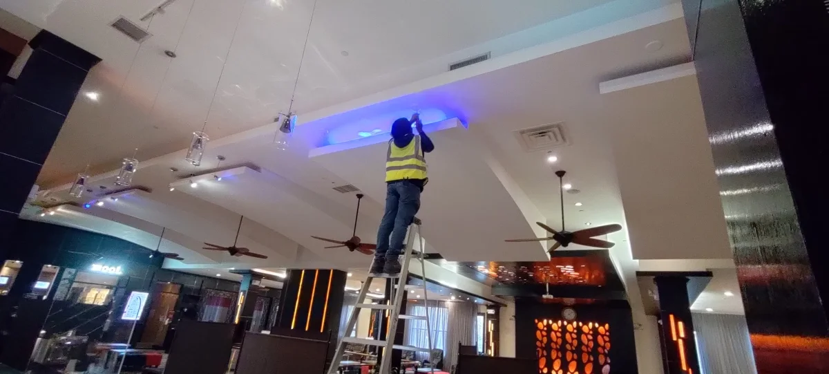 Electrician installing blue LED cove lighting above a commercial interior ceiling in New York City