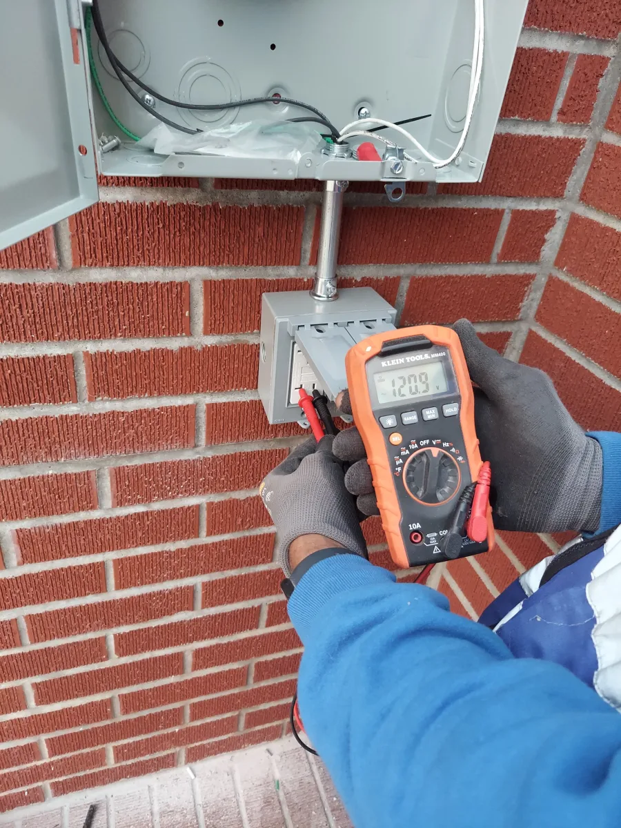 Electrician measuring voltage at a weather-protected outdoor receptacle during electrical troubleshooting in New York City